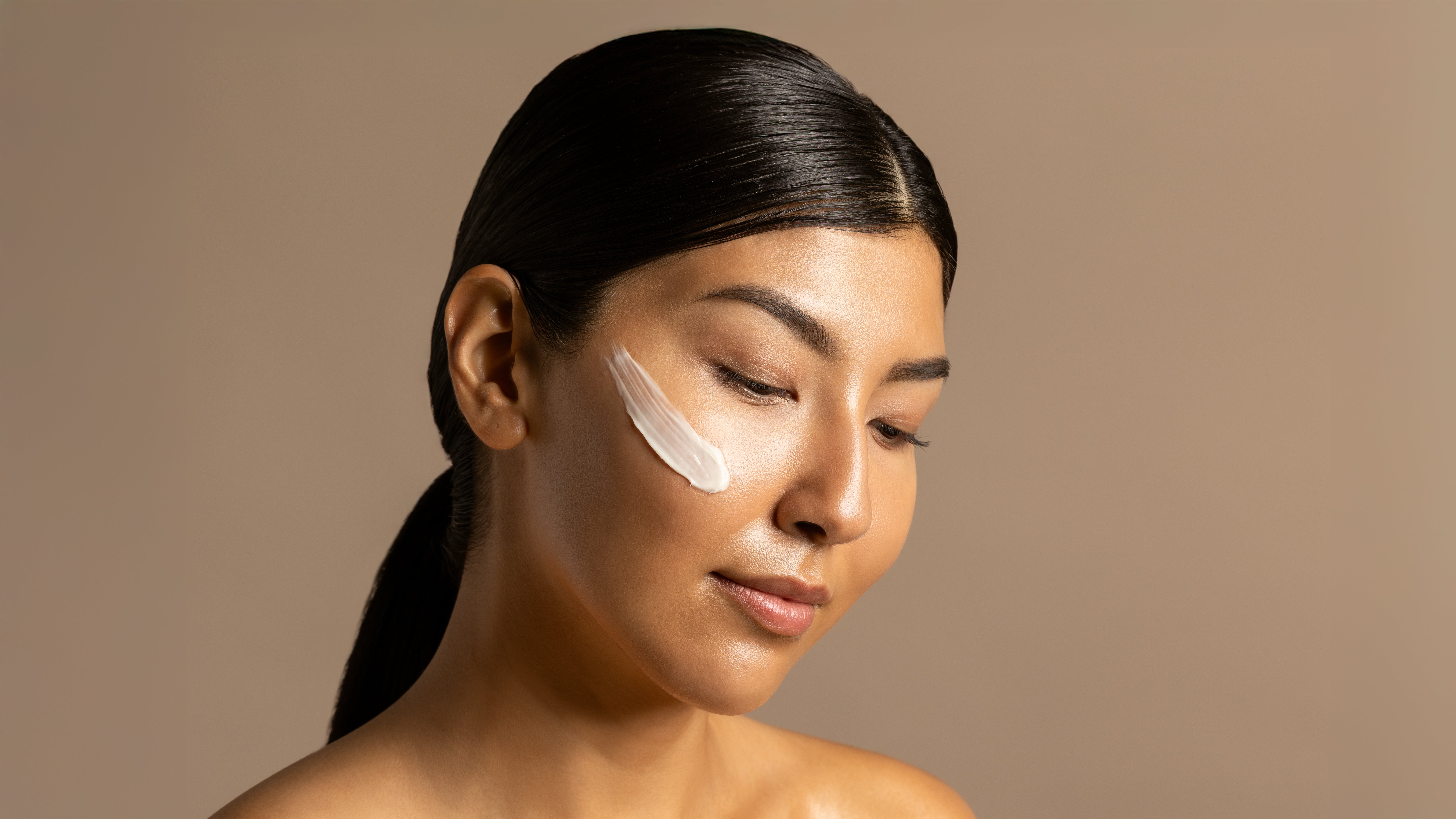 Woman with a skincare product applied to her face against a beige background